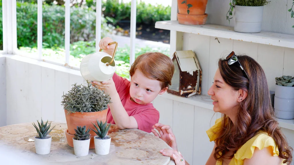 Toddler watering plants with parent encouragement, learning independence and stewardship in a Christian home.
