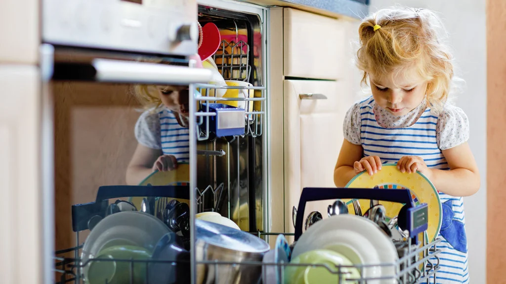 Toddler helping unload the dishwasher to practice responsibility and independence in a supportive, faith-based home environment.
