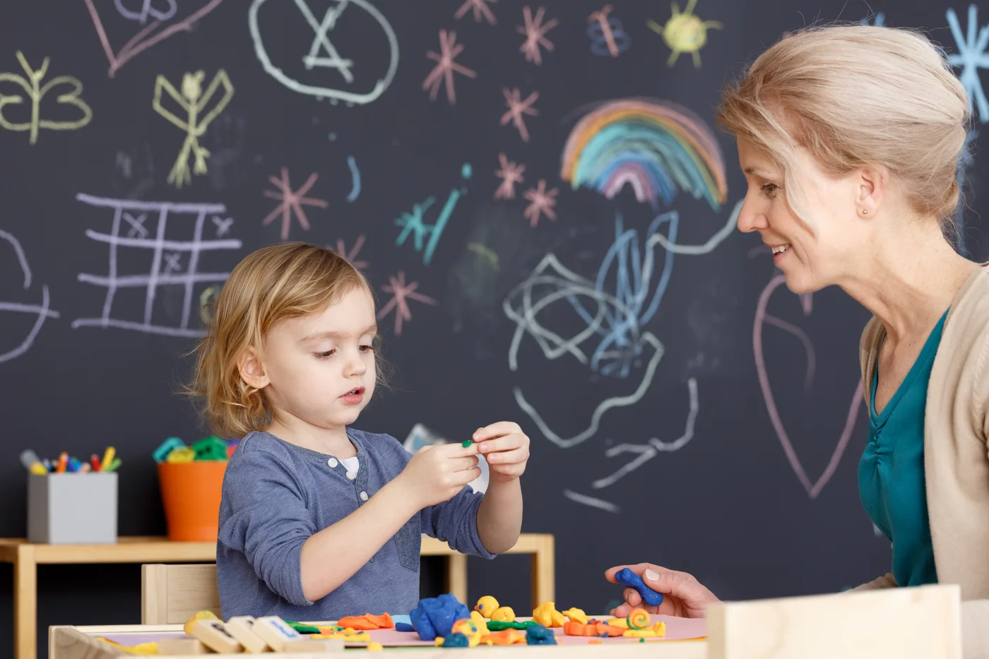 A young child exploring colorful hands-on materials beside a teacher