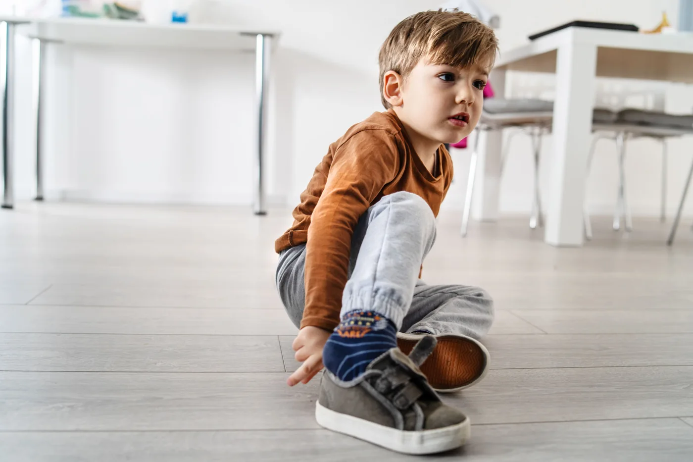 A young child sitting on the floor and putting on a shoe