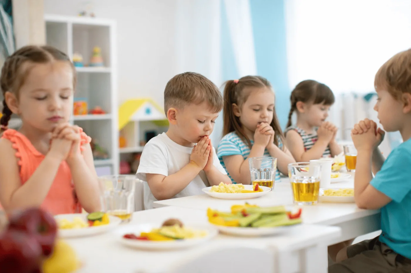 Children with hands clasped in prayer before a meal together