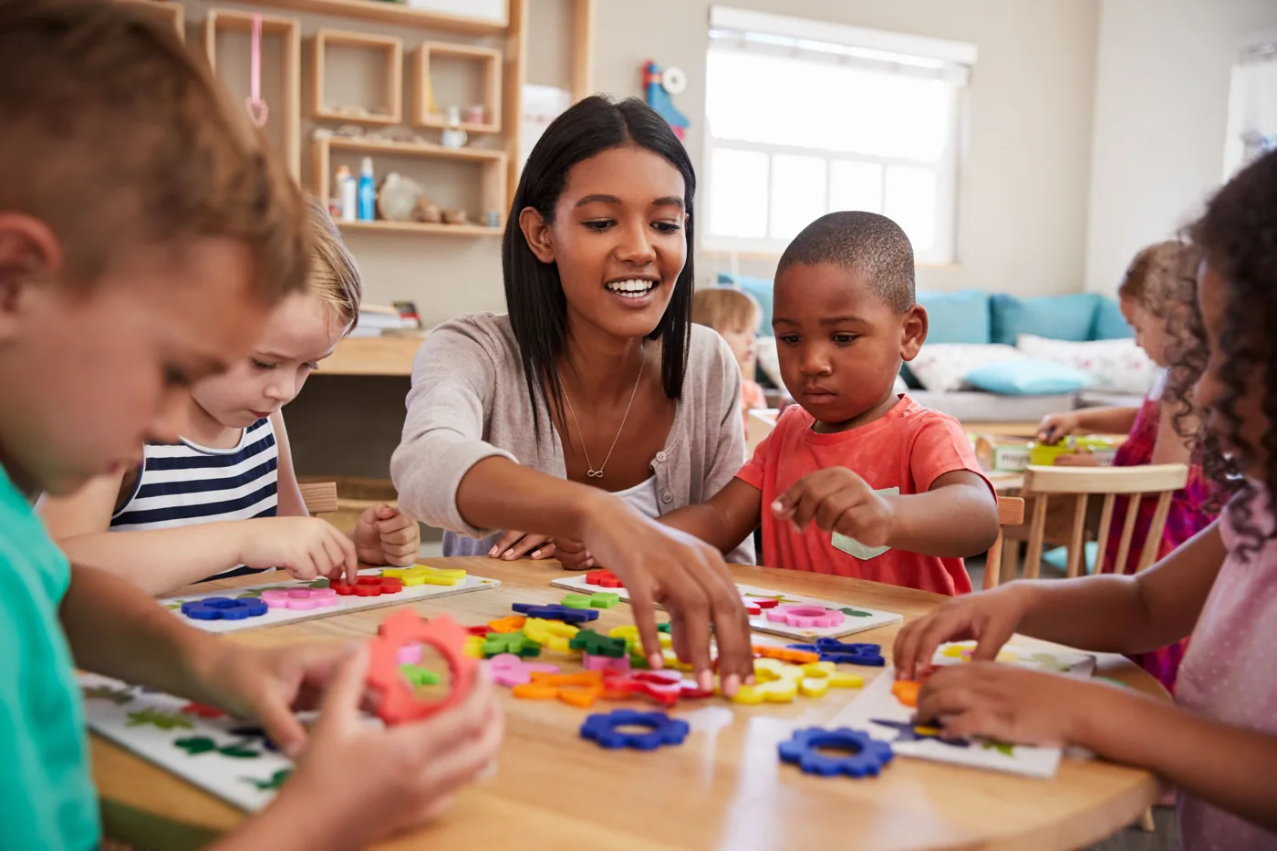 A teacher helping children explore colorful shapes around a classroom table