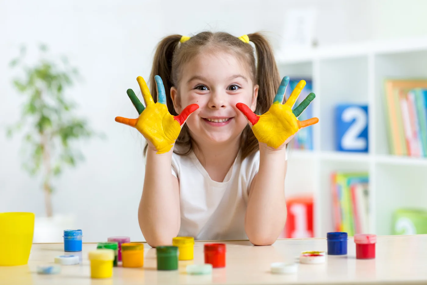A smiling child showing hands covered in colorful paint